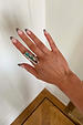 Chunky Deloris Whistle Ring with teal, green and red gemstones, styled on a hand with striped nail art.