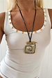 Deloris Mermaid Necklace featuring an engraved brass pendant on a black leather cord, styled on a white ribbed top.
