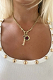 Iconic Deloris Key Necklace with a gold brass key pendant and red gemstone charm, styled on a model.