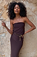 Multi-wear Chocolate Sabine Dress in brown stretch fabric, styled strapless against a stone wall and designed in London.