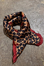 Thumbnail for Cherry Leopard Bandana featuring leopard print with red cherries and a deep red ruffle edge on a textured surface.