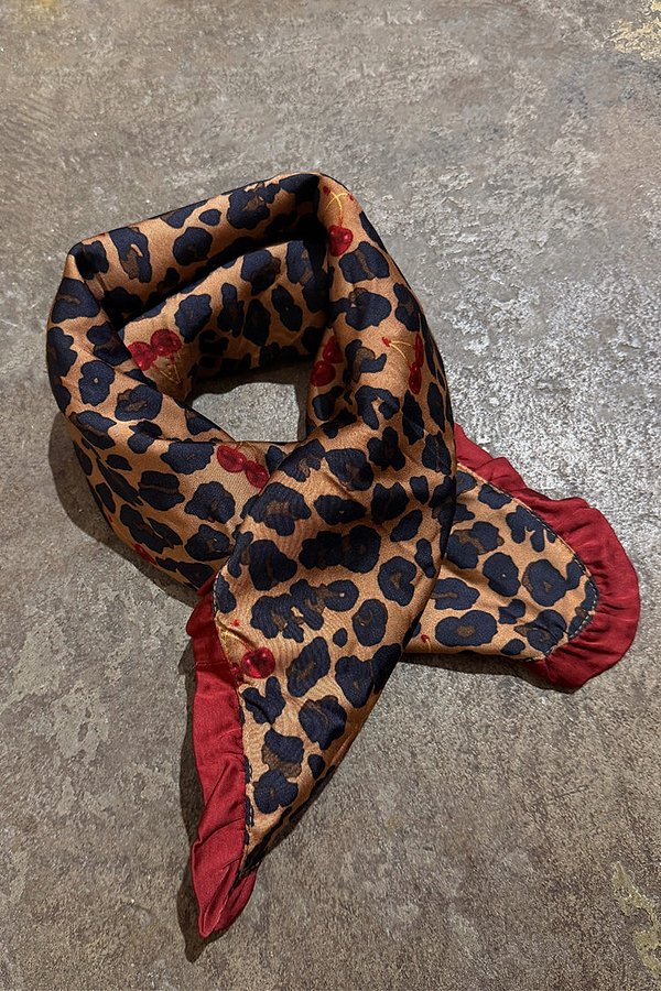 Cherry Leopard Bandana featuring leopard print with red cherries and a deep red ruffle edge on a textured surface.