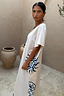 Cream cotton Dolce Vita T-Shirt Dress with blue sun motifs, shown on a model in a rustic courtyard.