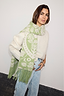 Olive Amara Knit Scarf featuring heart and eye motifs with a tasselled hem, styled over a cosy white jumper.