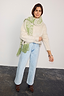 Olive Amara Knit Scarf featuring green heart motifs and a tasseled hem, worn with a cream jumper and light wash denim.
