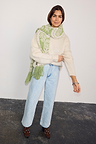 Olive Amara Knit Scarf featuring green heart motifs and a tasseled hem, worn with a cream jumper and light wash denim.