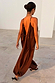 Chocolate Balloon Jumpsuit with a deep V back and draped silhouette, shown on a model walking outdoors.