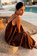 Chocolate Balloon Jumpsuit with a loose silhouette and deep V-back, worn by a model sitting on a woven stool poolside.
