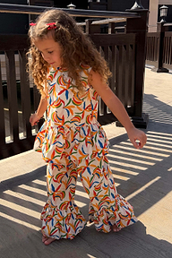NFD Kids cream cotton banana print co-ord with a peplum top and flared frill trousers on a sunny deck.