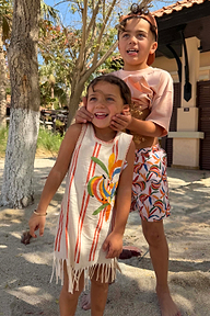 Cream Banana Jersey Cotton Dress with orange stripes and fringe hem, worn by a young girl on vacation.