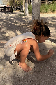 Girl's Banana Jersey Cotton Dress in cream with fringe hem detail, worn by a child playing in the sand.