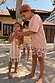 Boy's multi-coloured Banana Print Swim Shorts in recycled polyester, worn by children in a sunny vacation setting.