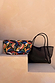 Black mesh tote bag with leather straps and a multi-coloured banana print pouch on neutral steps.