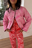 Reversible pink bandana quilted jacket with leopard trim and popper fastenings, styled with matching red trousers.
