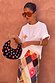 Black stone beaded crescent bag with multicoloured stones and a sculpted wooden handle, held against a warm-toned wall.