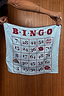 Blue Bingo Bandana with a red bingo grid print and iconic lip motifs, held up against a wooden backdrop.