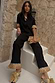 Thumbnail for Black Raffia Marra Trousers with a raffia fringe hem, styled as a co-ord on a model sitting on white stone stairs.