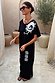 Black Dolce Vita cotton maxi dress with white sun motifs and Greek graphics in an outdoor terrace setting.