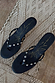 Black leather stud sandal mules with silver detailing and a gold sun motif, displayed top-down on a woven rug.