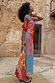Blue Dolce Vita Mesh Dress with vibrant red swirl motifs, styled with a beaded eye bag against a stone wall.