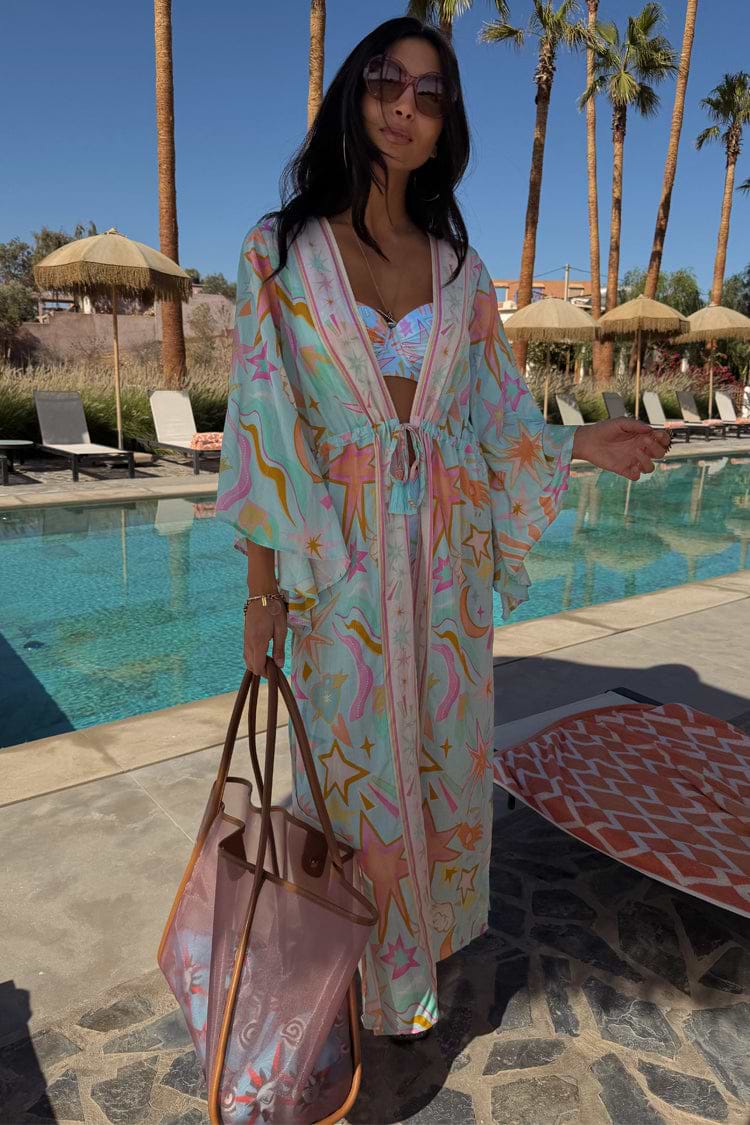 Blue Dreamer Maxi Kimono with a light blue celestial print, wide sleeves and tie waist in a poolside setting.