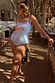 Blue Starburst print bandeau swimsuit with ruched ties, worn by a model in a sandy vacation setting.