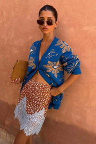 Blue Eye Cardigan with iconic sun and heart motifs, styled with a patterned lace skirt and sunglasses.