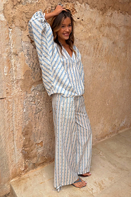 Blue and cream striped balloon trousers with gold studs and tie-cuffs, worn as a co-ord set against a stone wall.