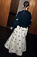 Thumbnail for Black Bow Sophie Cardigan with 3D cream bows, shown from the back with a tie-neck detail and bow-print maxi skirt.