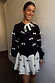 Thumbnail for Black Bow Sophie Cardigan with cream 3D bows and a tie neck, styled with a matching bow-print mini skirt.