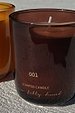 NFD Eau De Parfum Candle 001 in a burgundy glass jar with gold lettering on a sunlit stone surface.
