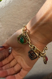 Brushed gold Deloris Charm Bracelet with chunky links and symbolic eye, spiral, and red stone charms on a person's wrist.