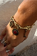 Deloris Charm Bracelet in brushed gold with key and eye motifs, featuring a red stone charm on a wrist.