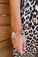Deloris Charm Bracelet in brushed gold with eye and mermaid charms, worn with a leopard print dress.
