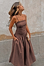 Chocolate Lola Mid-axi Dress in brown cotton with a ruched bodice and full skirt, posed against a stone wall.