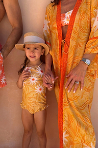 Yellow sun print swimsuit with frill details on a young girl wearing a straw hat on vacation.