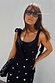 Black crochet Alicia dress with silver sequin details and tie straps, styled with sunglasses for a vacation.