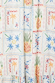 Island cross-stitch print on white cotton dobby fabric with pineapple, palm, and sun motifs.