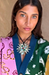 Gold Deloris Sun Necklace with semi-precious stones and a black leather cord, worn over a colourful knit cardigan.