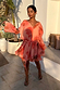 Blurred Floral Ella Mini Dress in peach orange with tiered ruffles and flute sleeves, styled outdoors.