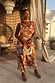 Star Fawn Sophie Dress in brown with sun and palm motifs and a multi-wear neck scarf on a model.