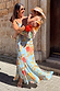 Sky Blue Floral Sofia Dress with tie-knot shoulders and a bias-cut, shown on a model holding a child in a sunlit setting.