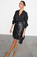 Black vegan leather mini Jaspre wrap skirt with fringe detailing, styled with a black blouse and textured clutch.