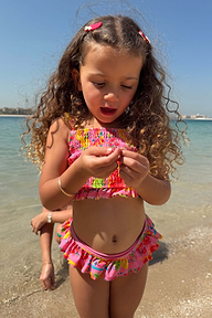 Girls Pink Fruit Crop Bikini Set with a Mediterranean fruit print, shirred bandeau top and frill bottoms at the beach.