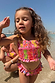 Girls Pink Fruit Crop Bikini Set with a shirred bandeau top and frill bottoms on a girl at the beach.