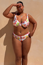 Fruit Stamps bikini bottoms featuring pink whipstitch trim and a Mediterranean fruit print on a curve model.