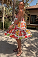 Fruit Stamps Mini Dress featuring a Mediterranean-inspired fruit print and tiered skirt in a sunny outdoor setting.
