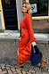 Giraffe Emma Dress Petite with an orange crochet knit top and printed skirt, walking along a cobblestone street.
