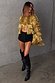 Gold metallic fringe jacket with layered foil tassels, styled with black shorts and knee-high leather boots.