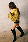 Gold Fringe Jacket featuring layered gold foil tassels, styled with black knee-high boots and shorts.